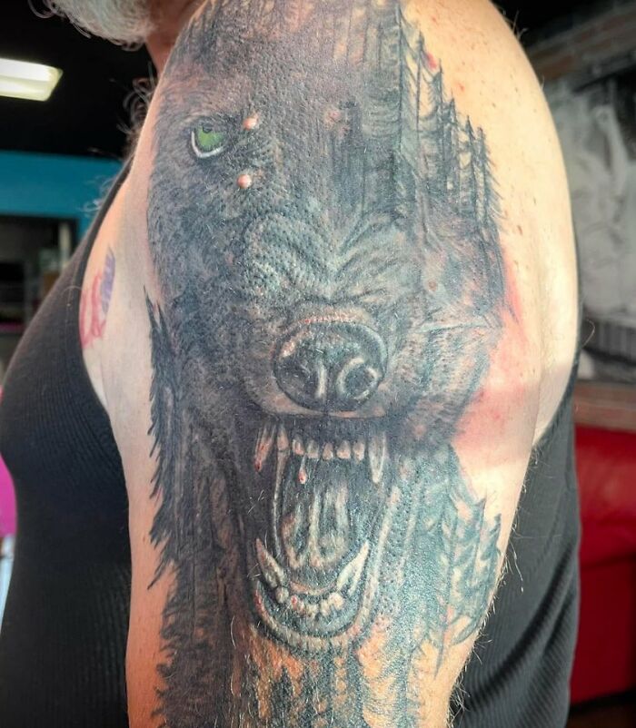 Close-up of a detailed wolf tattoo on upper arm, showcasing intricate shading and a green eye in a unique body tattoo design.