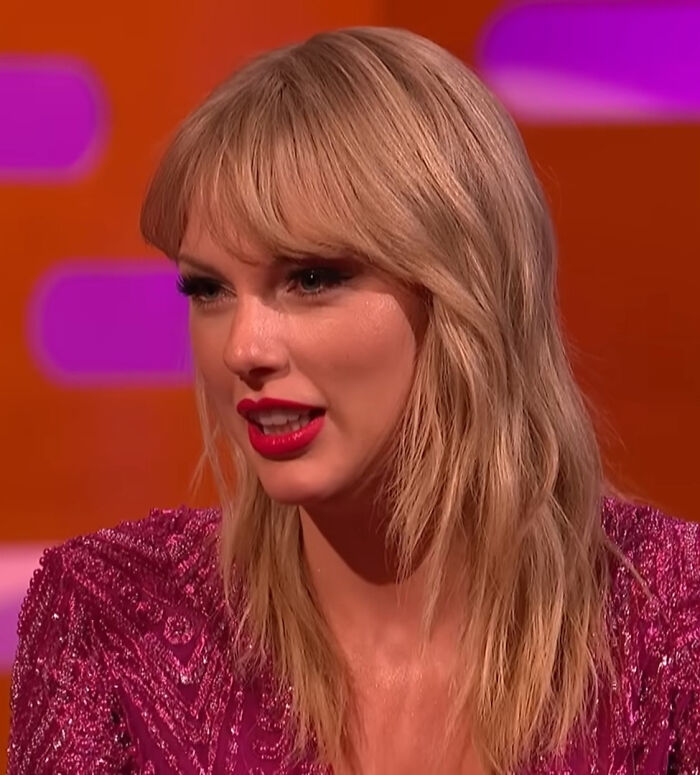 Taylor Swift wearing a sparkling purple outfit with blonde hair, styled amid album release reactions and Caitlyn Jenner comparisons.