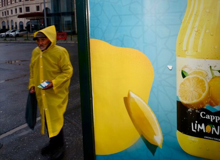 Man in yellow raincoat walking past a bright lemon beverage advertisement on the wet streets of Istanbul.