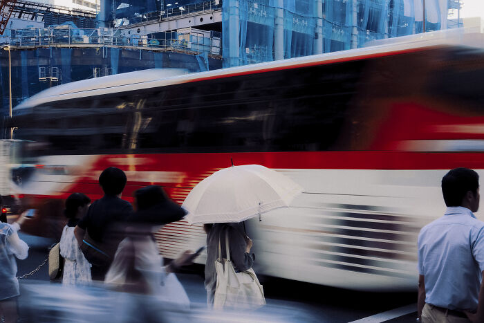 Blurred street photography shot of people crossing near a red and white bus, capturing life’s unexpected moments in the city.