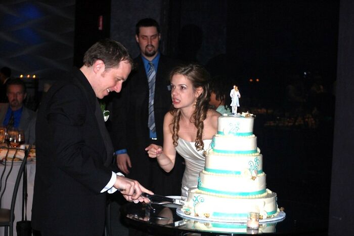 Bride looking annoyed at wedding guests while groom cuts cake, illustrating wedding guests causing regret for bride and groom.