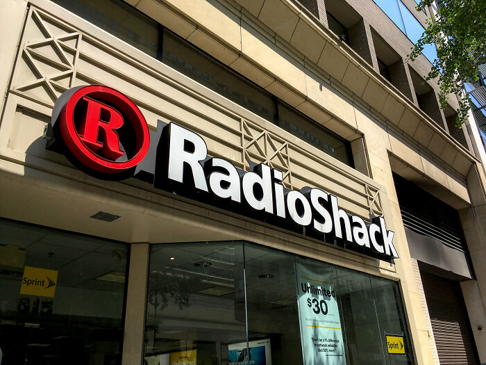 RadioShack storefront with a large sign above the entrance, featuring branding and promotional posters inside the glass window.