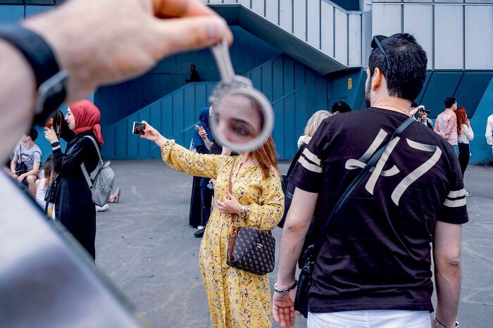 Busy life on Istanbul streets captured with a woman’s face reflected through a handheld mirror in the foreground.