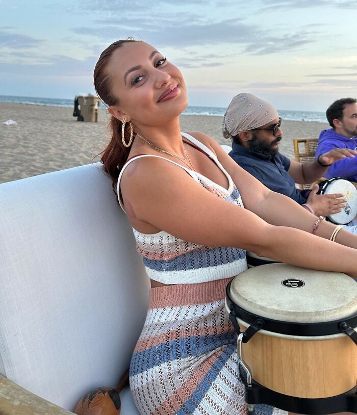 Young woman playing a drum on the beach, fans suspicious of Selena Gomez kidney donor amid wedding drama.