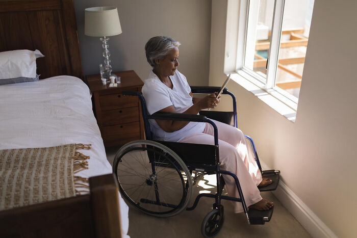 Elderly woman in a wheelchair using a tablet by the window, reflecting moments of unfiltered and funny dementia patient quotes.