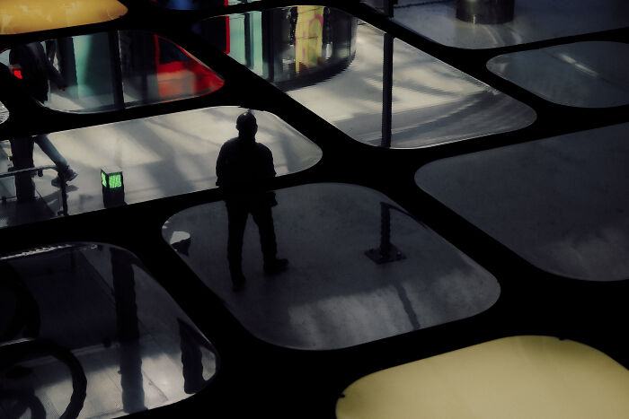 Silhouetted person standing on reflective floor with colorful lights, a stunning street photography shot capturing life’s moment.