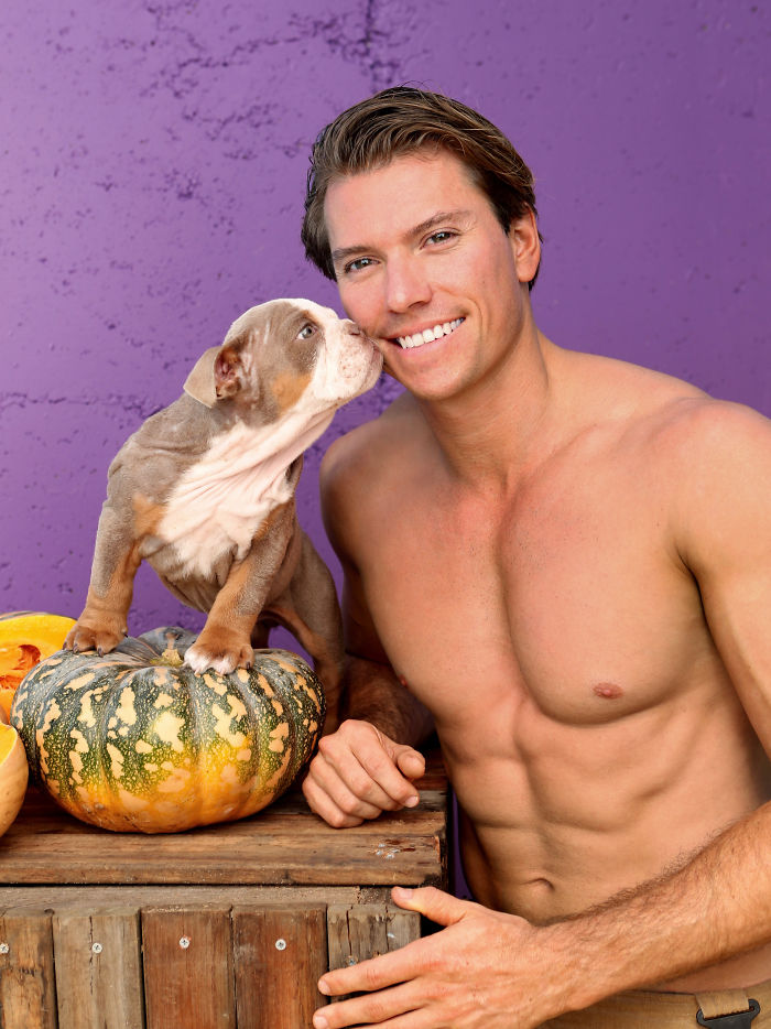 Shirtless man smiling as an adorable dog stands on a pumpkin, showcasing heroic firefighters and adorable dogs theme.