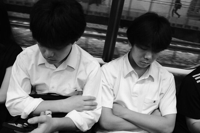 Black and white street photography of two young men sitting with arms crossed, capturing life’s unexpected moments on a subway.