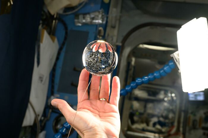 Hand holding a floating water sphere in microgravity, demonstrating the beauty and mystery of space exploration.