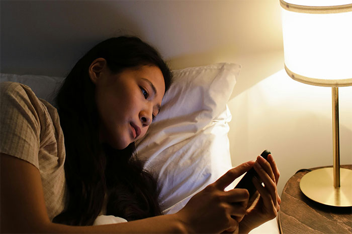 Woman lying in bed looking concerned at her phone, illustrating fallout over unvaccinated kid discussion.