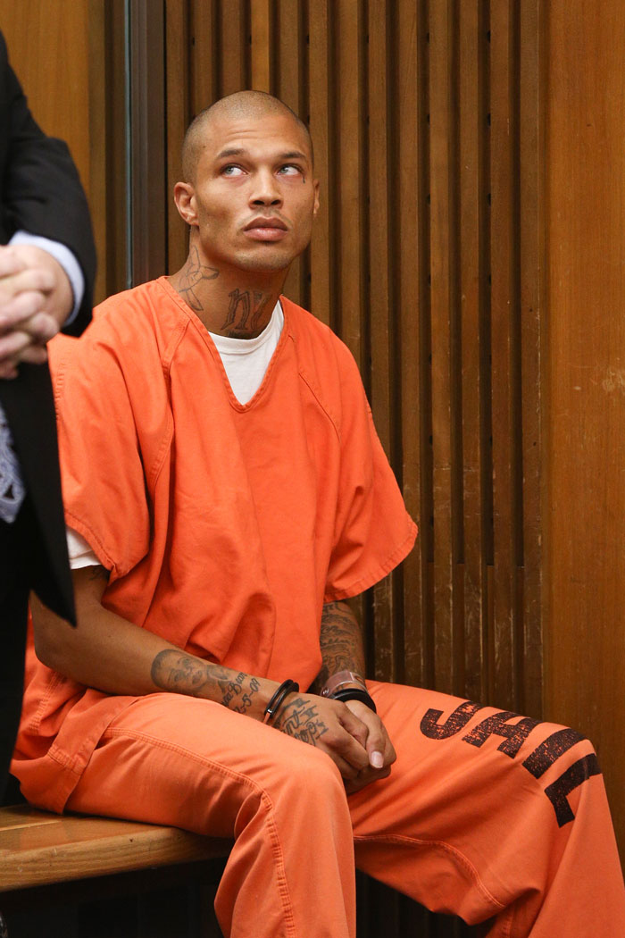 Man known as world's hottest felon wearing orange jail uniform with tattoos, sitting in courtroom looking upward
