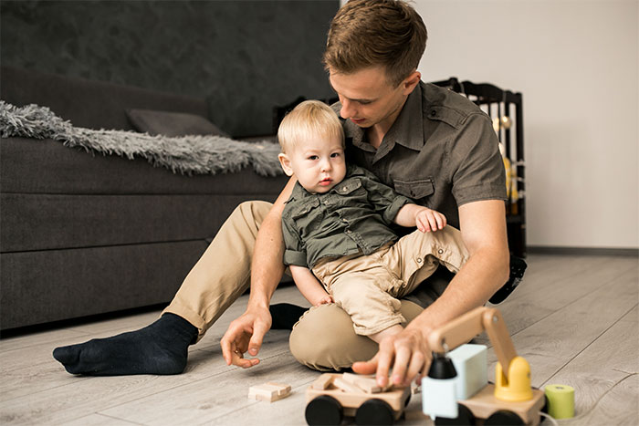 Young father playing with toddler son on floor, symbolizing woman expects help from ex-husband after leaving him for another man.