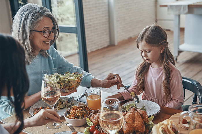 Family sharing a Thanksgiving meal, with focus on a woman serving salad to a young girl at the dining table. Family sharing a Thanksgiving meal, with focus on a woman serving salad to a young girl at the dining table.