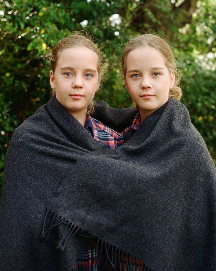 Twin sisters wrapped together in a dark blanket, captured in a stunning portrait by a London photographer.