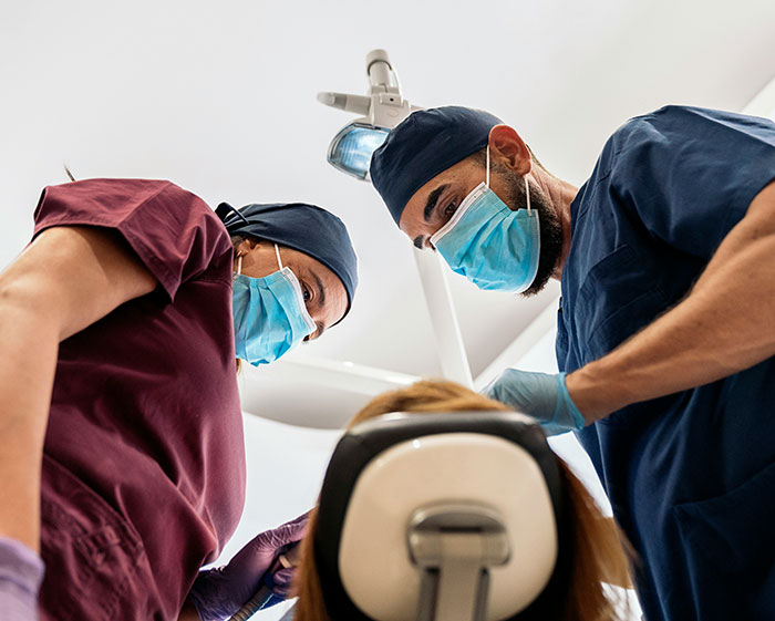 Two dentists wearing masks and scrubs performing a tooth removal on a patient in a dental clinic.