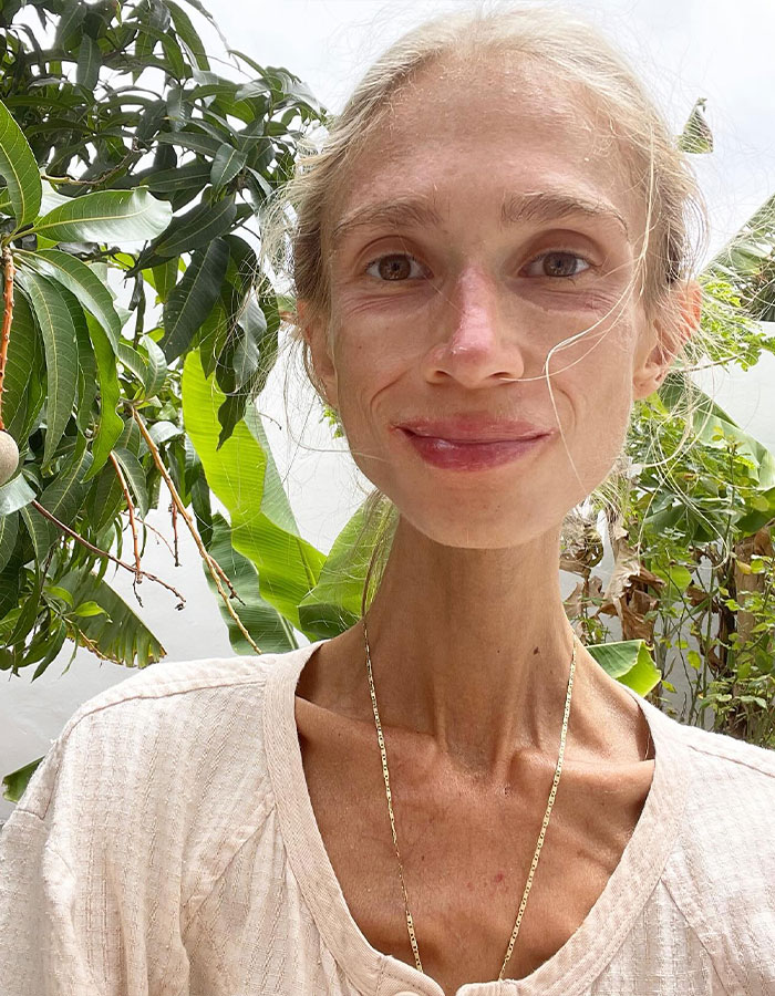 Vegan woman with a thin frame and light-colored shirt posing outdoors near green leafy plants. Vegan woman with a thin frame and light-colored shirt posing outdoors near green leafy plants.
