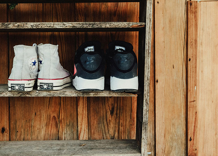 Pair of old sneakers and worn shoes placed neatly on a rustic wooden shelf, showcasing everyday life hacks organization.