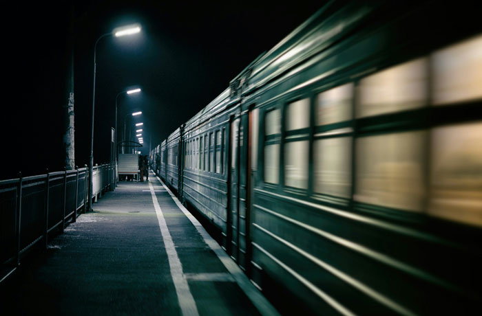 Nighttime view of a moving train at a deserted station platform, evoking wild urgent stories about needing to leave immediately.