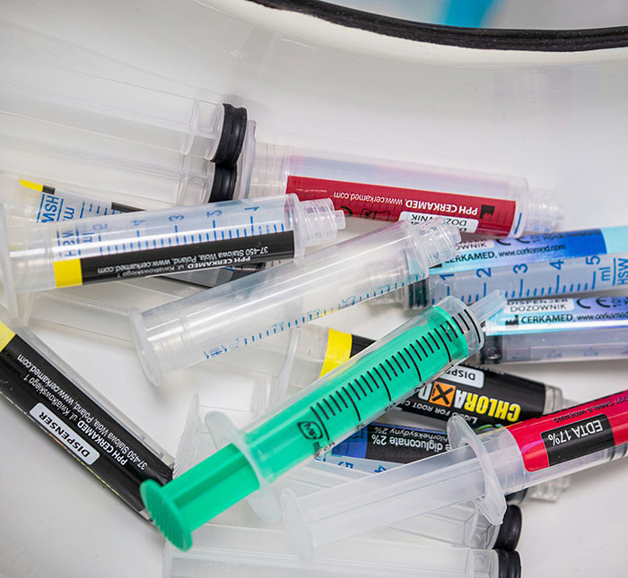 Multiple empty syringes with colorful labels scattered on a white surface, related to influencer's fake syringe attack pranks.