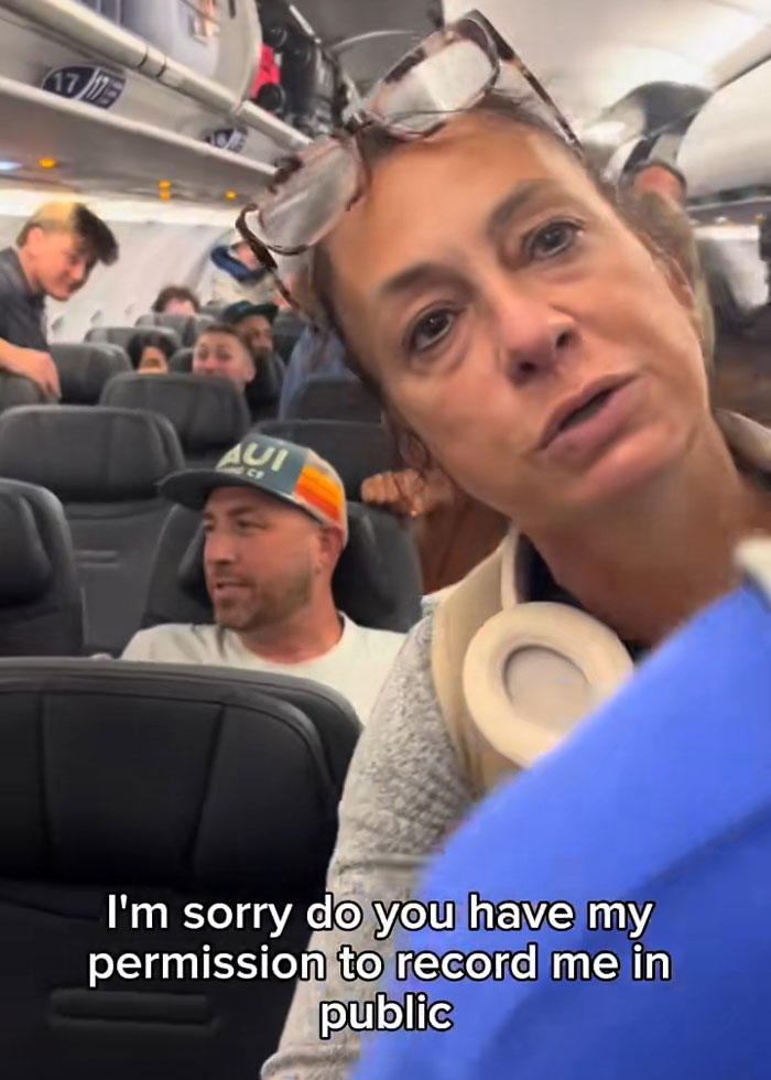 Woman confronts passengers on plane with headphones around neck, scene captures tense moment during in-flight dispute. Woman confronts passengers on plane with headphones around neck, scene captures tense moment during in-flight dispute.