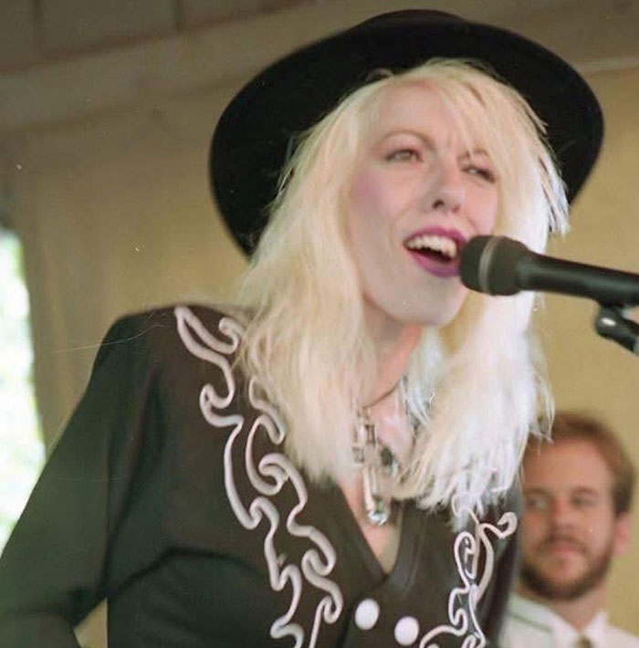 Dolly Parton's sister singing at a microphone, wearing a black hat and embroidered black shirt during a live performance.