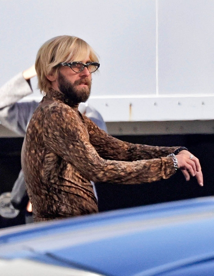Jonah Hill with blonde hair and beard wearing glasses and a patterned brown shirt showing major transformation outdoors.