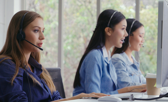 Three women wearing headsets working at computers in an office, illustrating unexpected and awkward work moments.
