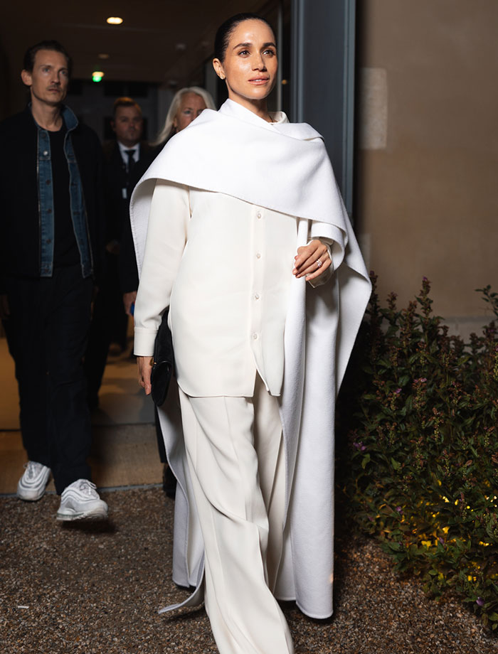 Meghan Markle attending Paris Fashion Week in an elegant white outfit, captured at a nighttime event.