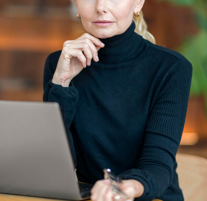 Woman in black turtleneck seated at laptop, appearing thoughtful while discussing horrifyingly cruel person experiences.