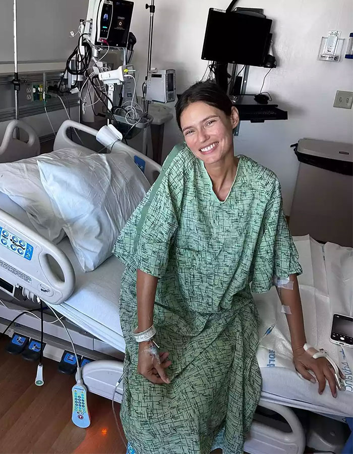 Former Victoria&rsquo;s Secret model in hospital gown smiling while receiving treatment, highlighting cancer battle and show rejection.