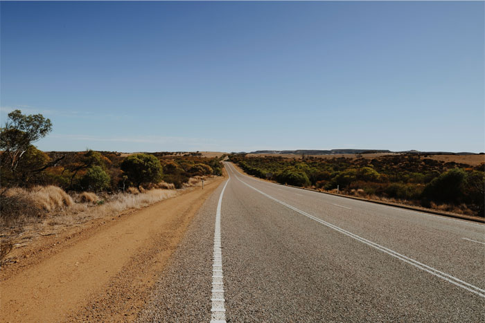 Empty rural road stretching through dry landscape under clear blue sky, related to insurance coverage denial incident.