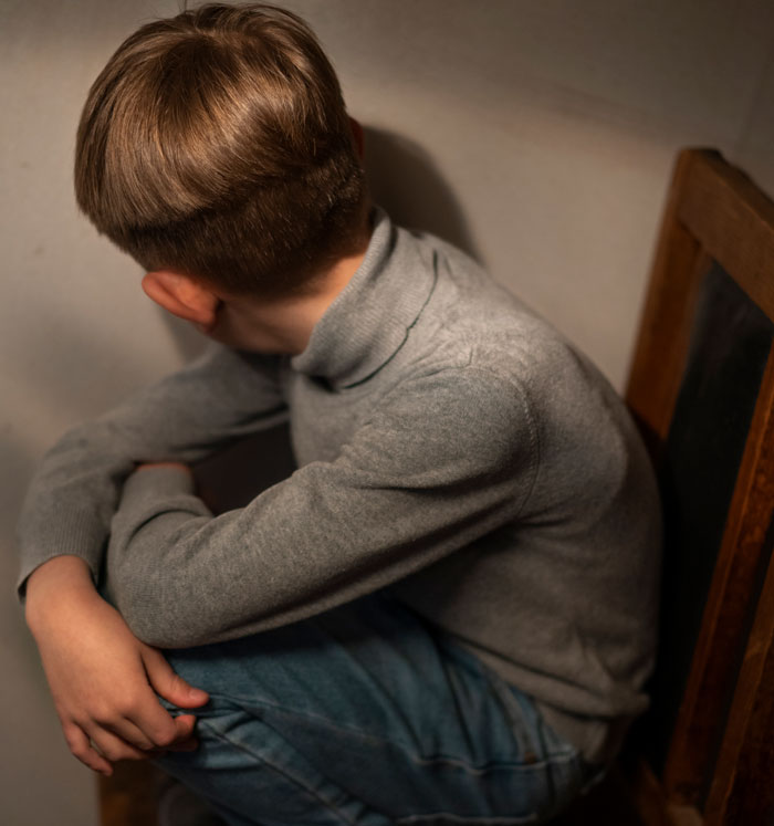 Young boy sitting alone on a wooden chair, looking away, illustrating the impact of worst crimes in their hometowns.