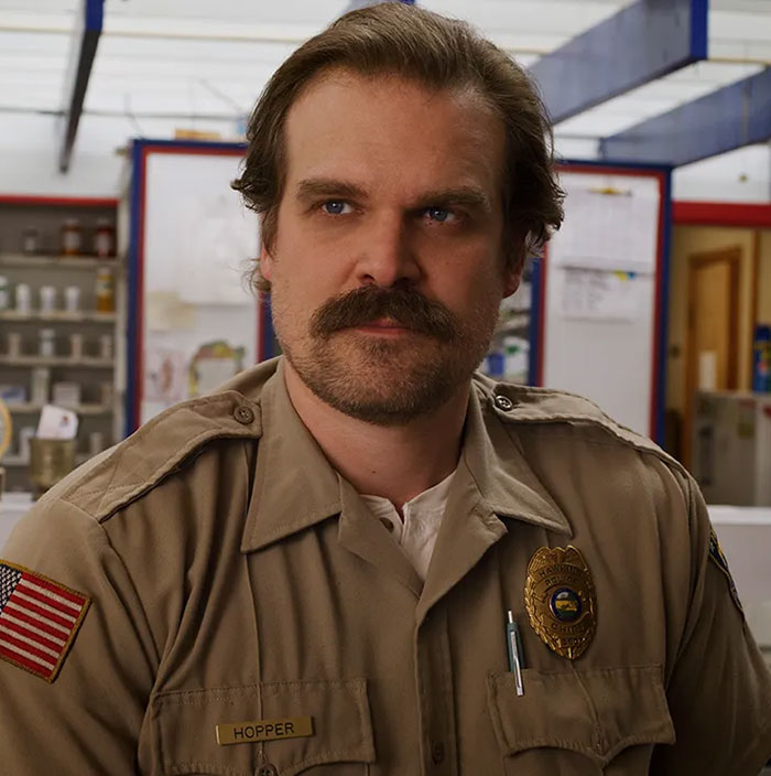 David Harbour in police uniform as Hopper, fans clash online over whether he deserves to be fired for cheating claims.