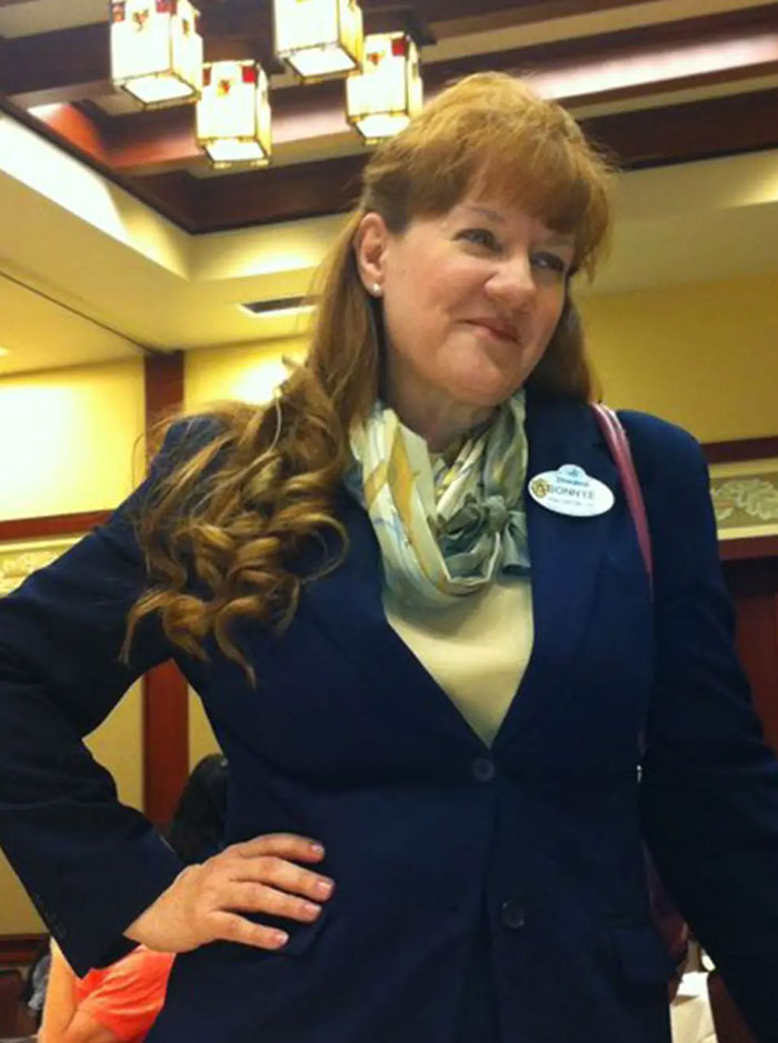 Woman in a navy blazer and scarf wearing a Disney World name badge indoors with warm lighting overhead