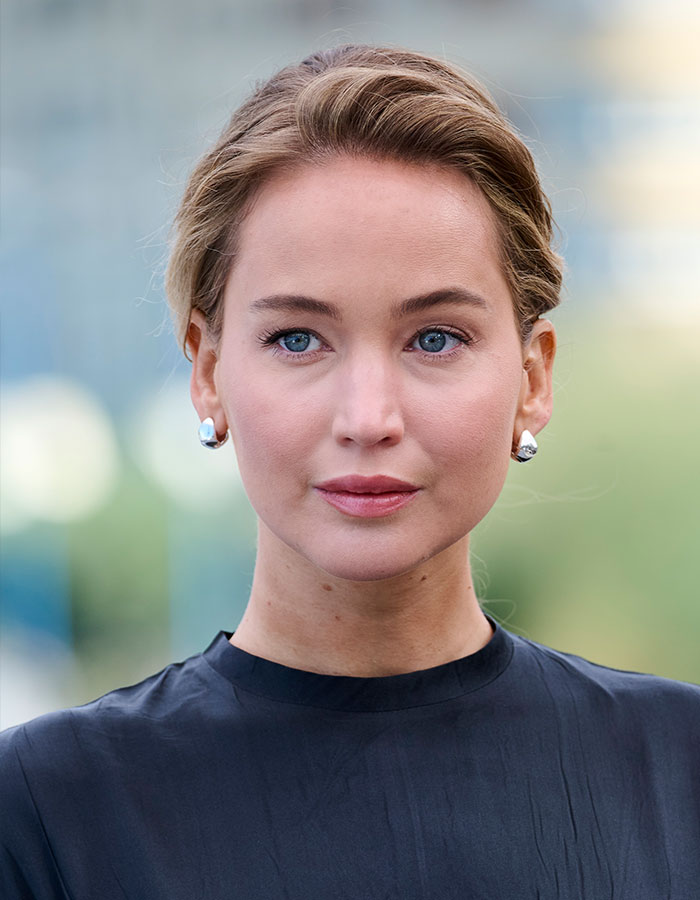 Jennifer Lawrence close-up portrait with natural makeup, earrings, and hair pulled back, addressing plastic surgery plans.