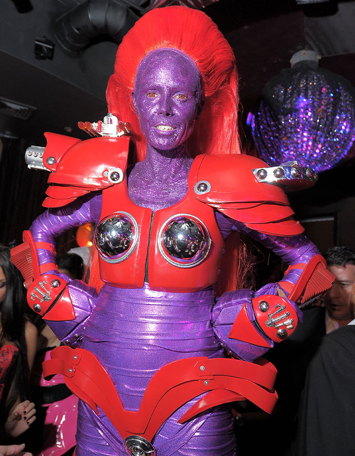 Person dressed in a nightmare-level 2025 costume with purple glitter skin and red armor at a Halloween event.