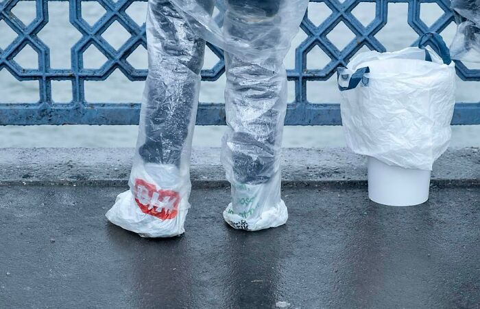 Person wearing plastic covers on shoes standing by ornate railing on Istanbul streets on a rainy day
