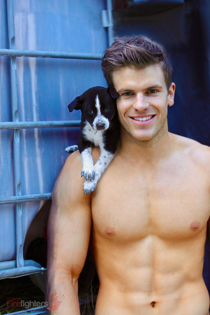 Shirtless Australian firefighter smiling with a small black and white dog perched on his shoulder.