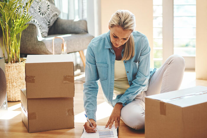 Woman sitting on floor among moving boxes, organizing and labeling items to zip-line your boxes out efficiently.