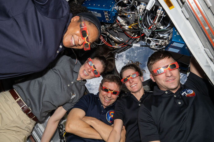 Five astronauts inside a spacecraft wearing protective glasses, showcasing the beauty and mystery of space exploration.