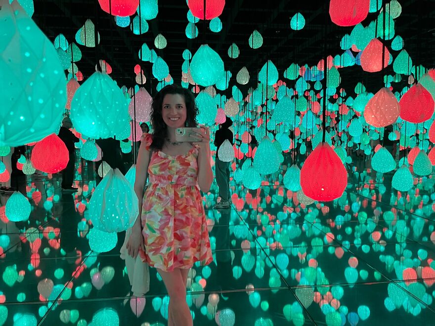Woman taking selfie in colorful illuminated room filled with hanging lights, representing woman getting responses after billboard campaign.