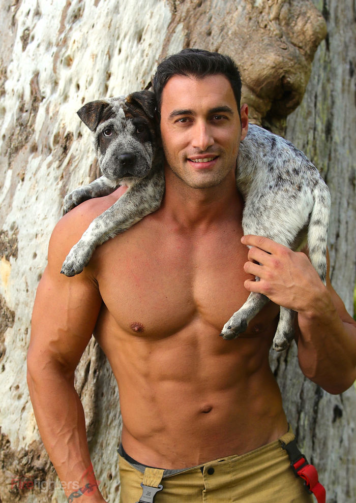 Shirtless heroic firefighter posing outdoors with adorable spotted dog draped over his shoulders for Australian calendar.