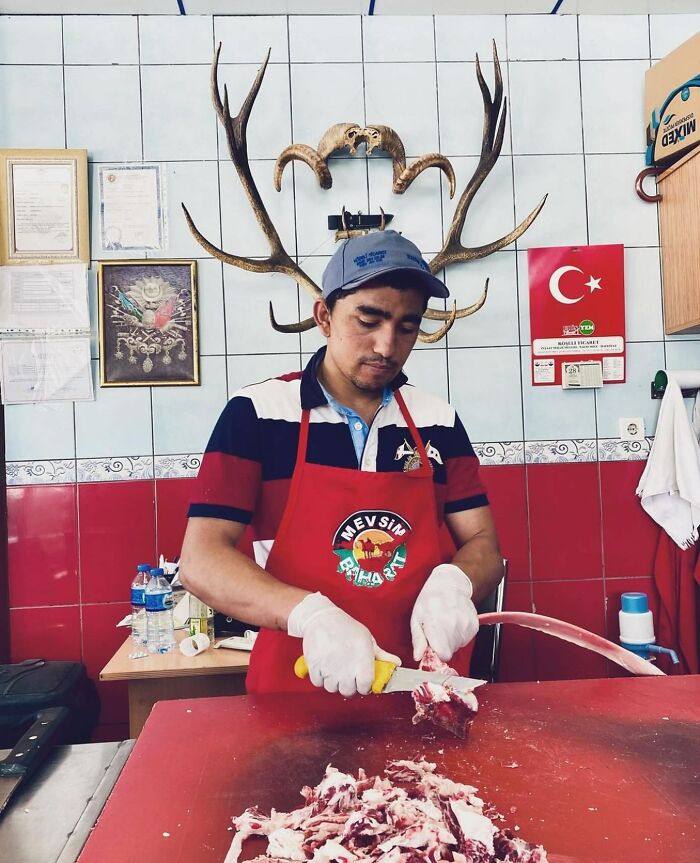 Man in an apron carving meat at a butcher shop, showcasing daily life on Istanbul’s streets with local details visible.