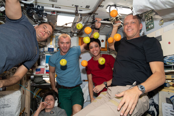 Astronauts floating with fruit inside a spacecraft, showcasing the beauty and mystery of space in astronomy photos.
