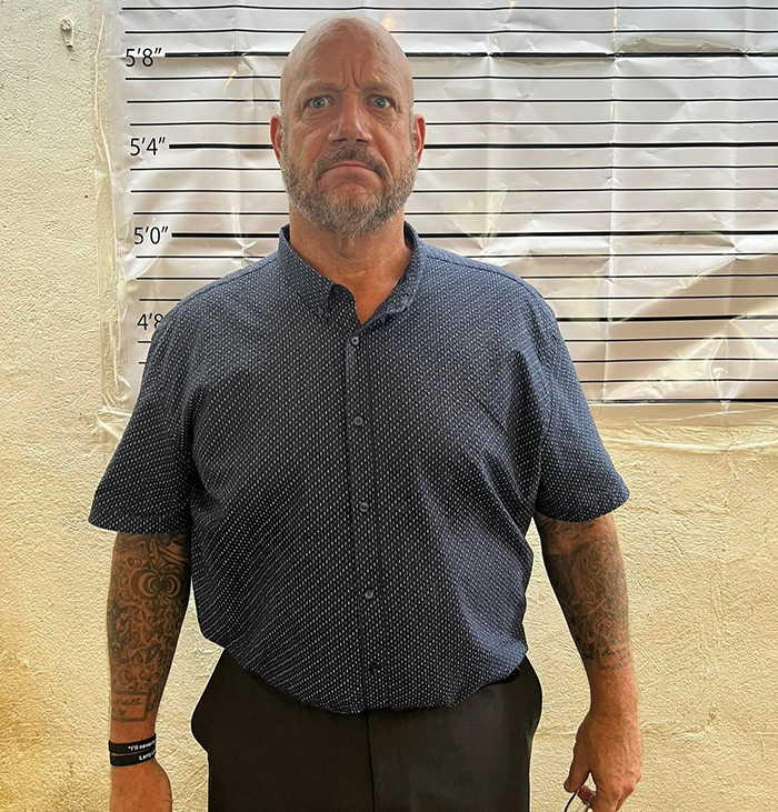 Middle-aged man with tattoos stands in front of height chart, representing America&rsquo;s most notorious jewel thief.