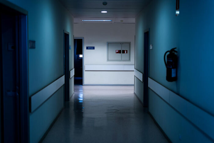 Dimly lit hospital corridor at night with closed doors and a fire extinguisher, evoking scary ghost stories hospital work.