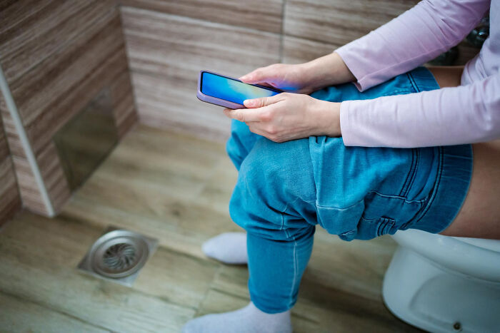 Person sitting on a toilet with jeans down, holding a smartphone, illustrating hilariously painful moments of misreading social cues.
