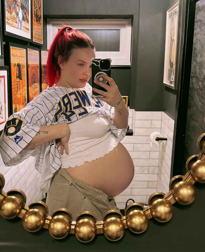 Pregnant pop star taking a mirror selfie in casual clothes, raising questions about diabetes and baby naming choices.