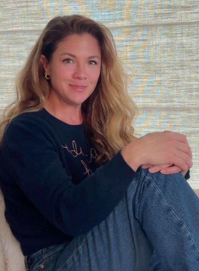 Woman with long blonde hair sitting casually in a dark sweater and jeans, relating to Katy Perry and Justin Trudeau romance news.