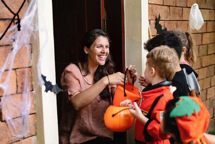 Woman handing out candy to kids in costumes, capturing hilariously painful moments of misreading social cues during Halloween.